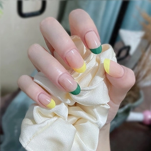 Detail of nude French tip press-on nails with green and yellow edges on a silk scrunchie