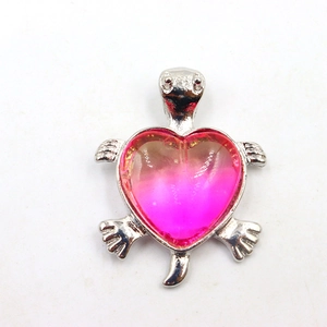 Detailoverzicht van zilveren schildpadhanger met roze kristallen hart op witte achtergrond