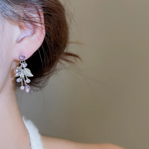 Detail of silver leaf earring with purple rhinestones on model showing high-end jewelry texture