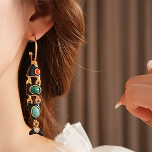Detail of vintage fish earring with colorful stones and gold frame on model's ear