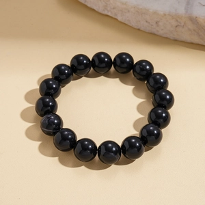 Macro detail of polished black acrylic beaded bracelet on a textured stone surface