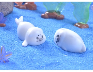 Macro shot of two white miniature seal figurines on a blue sand micro landscape