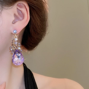 Macro shot of elegant purple teardrop crystal earring with intricate gold diamond setting