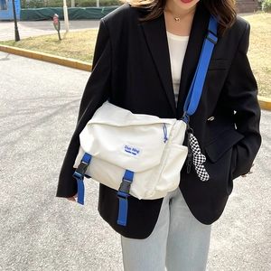 White nylon crossbody messenger bag with blue webbing strap and checkered pendant charm