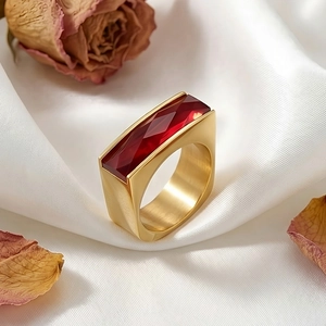 Macro detail of gold stainless steel ring with emerald-cut deep red gemstone on silk