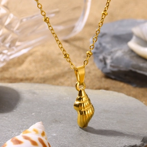 Close-up of golden shell pendant on beach sand with sea shells and stones