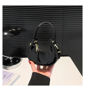 Detail of glossy black patent leather finish and golden metal buckle on a mini handbag