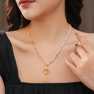 Collier de perles doré avec pendentif feuille d'érable porté sur un haut noir
