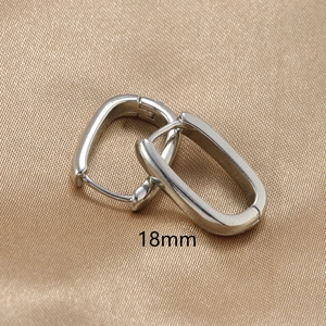 Macro shot of 18mm silver U-shaped earrings on elegant champagne satin fabric
