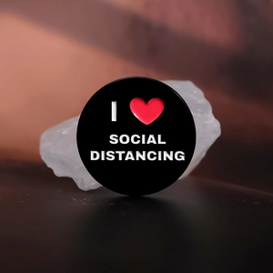 Dettaglio della spilla smaltata I Love Social Distancing su una pietra bianca decorativa