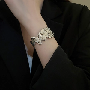 Detail of silver irregular crumpled texture cuff bracelet worn over a black blazer sleeve