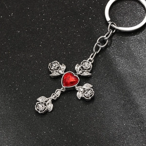 Macro detail of gothic cross keychain with red heart crystal and rose carvings
