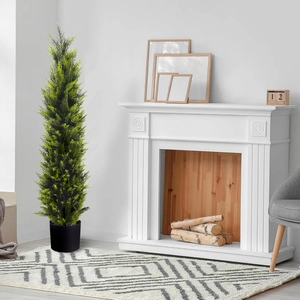 Tall artificial cypress tree in black pot placed next to a modern white fireplace
