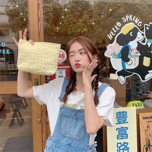 Asian model holding a yellow plaid fabric cosmetic bag in a sunny outdoor cafe setting