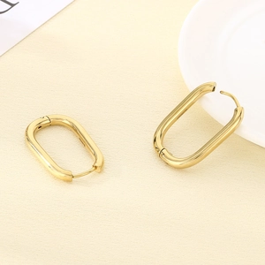 Detail view of oval gold U-shaped earrings on a textured surface with professional lighting