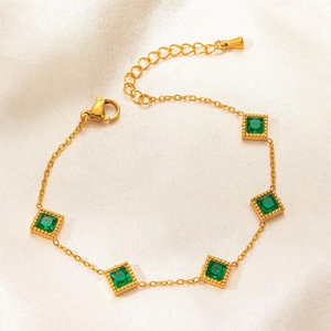 Detailed macro view of gold chain bracelet featuring square emerald green gemstones on silk