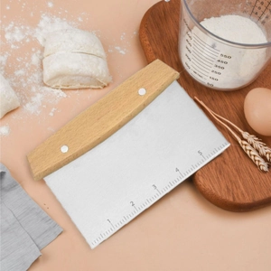 Flat lay of a stainless steel dough scraper with wooden handle and scale on a peach background