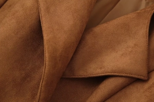 Detailed close-up of brown suede jacket fabric showing fine texture and precision stitching