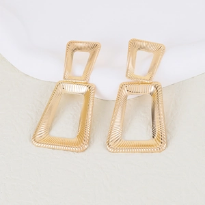 Golden geometric earrings with textured double rectangle design on white silk background