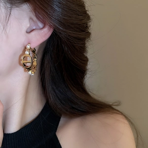Close-up of gold hoop earrings with white pearls and luxury logo detail worn by a model