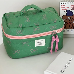 Green quilted cosmetic bag with pink bow pattern and top handle for travel storage