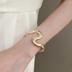 Close-up of minimalist gold wavy cuff bracelet on wrist showing elegant metallic texture