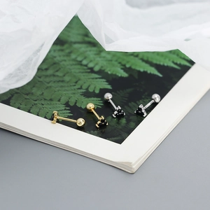 Macro detail of gold and silver clover stud earrings with black screw-back on plant background