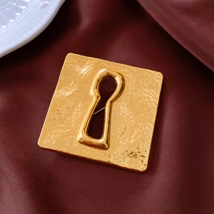 Macro detail of vintage gold square brooch featuring hammered texture and keyhole cutout