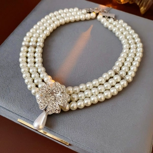 Macro detail of triple-layer pearl necklace with diamond clover clasp on grey velvet case
