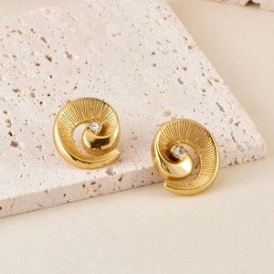 Elegant gold spiral stud earrings with center crystal on natural stone background