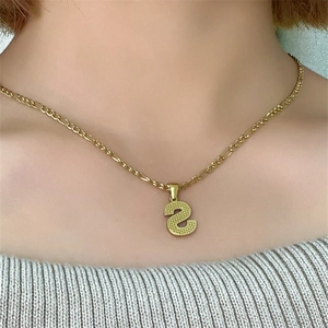 Dettaglio di una collana a catena Figaro dorata con un pendente a lettera S minimalista