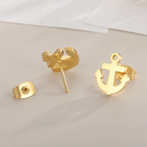 Macro detail of gold anchor stud earrings with metal butterfly backings on gray surface