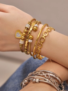 Detalle de brazaletes apilados de oro y plata con colgante de corazón de cristal