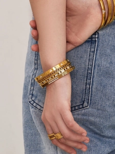 Gros plan de bracelets dorés superposés avec zircons et bague florale sur fond de denim