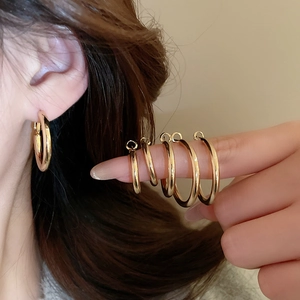 Set of minimalist golden hoop earrings in five different sizes shown on hand and ear