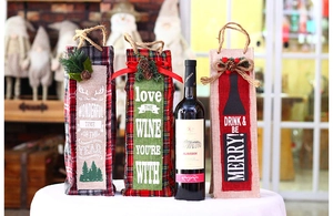 Close-up of linen Christmas wine gift bags with pine cone accents and festive typography