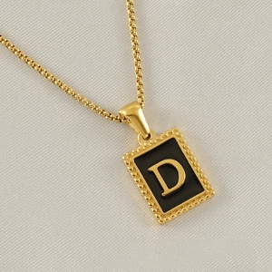 Macro detail of a gold rectangle pendant with black enamel and a 3D golden letter D