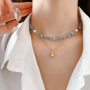 Detail of layered necklace with light blue stones, small pearls and a gold pendant