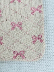 Detail of beige knit tote bag with pink bow pattern showing soft textured fabric