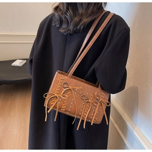 Detail of brown PU leather shoulder bag featuring woven strings, bows, and silver rivets