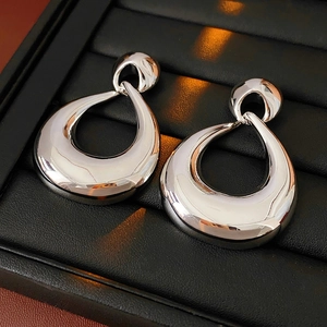 Macro shot of silver-colored teardrop earrings on a luxury black leather tray