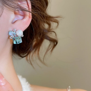 Detailed view of light blue square gemstone earring with pearl and diamond bow on a model