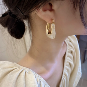 Close-up of elegant gold U-shaped earrings with white resin inlay worn by a model