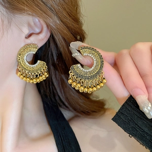 Detail of vintage C-shape crescent earrings with hollow carvings and beaded tassels