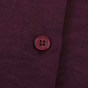 Detail eines lila Knopfes mit vier Löchern auf glänzendem Satin-Blusenstoff