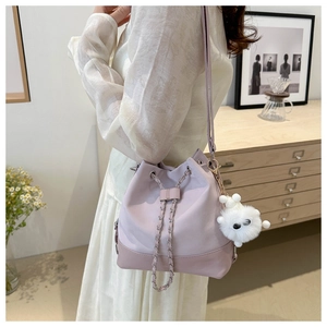 Detail of lavender bucket bag with metal chain and plush doll charm on shoulder strap