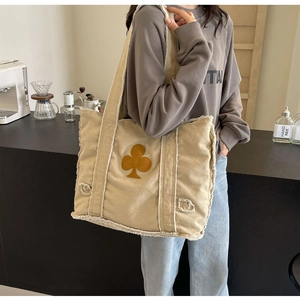 Detail of beige canvas tote bag with frayed edges and brown clover patch on model