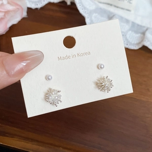 Detail view of silver snowflake and white pearl stud earrings on a lace fabric
