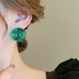 Détail macro d'une boucle d'oreille boule en résine verte transparente sur un mannequin