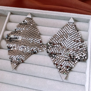 Détail macro de boucles d'oreilles triangulaires en maille argentée sur plateau